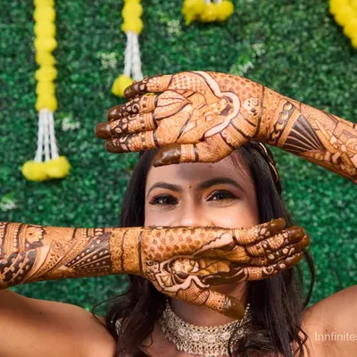 A playful portrait of the bride peeking over her hands, which are covered in elaborate mehndi. This shot highlights the beautiful henna work in a fun and engaging way.