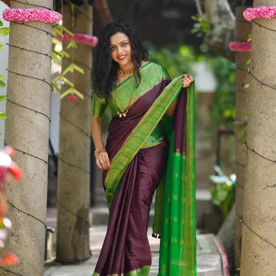 A beautiful portrait of a woman in a stunning purple and green silk saree, taken outdoors in a traditionally styled location.