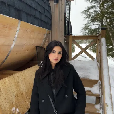 A classic winter portrait in an all-black outfit against a snowy cabin backdrop in Parry Sound.
