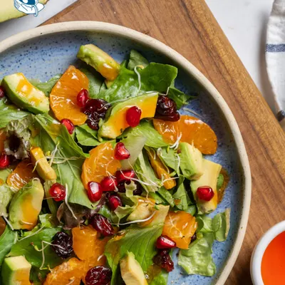 A feast for the eyes and the palate. This vibrant salad features mixed greens, creamy avocado, juicy mandarin oranges, tart cranberries, and a sprinkle of pomegranate seeds.