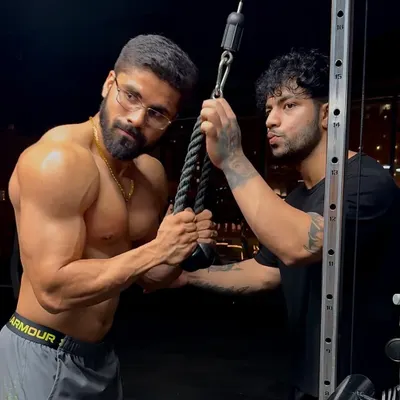 In the gym, providing hands-on correction for a tricep pushdown. Proper form is non-negotiable for maximizing muscle growth and preventing injury.