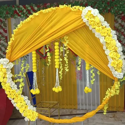 A close-up of a circular Haldi backdrop, showing how yellow fabric is draped within the frame and accented with marigold and white flower garlands.