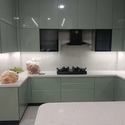 A wider view of the sage green modular kitchen, showing the U-shaped layout and the seamless integration of the breakfast counter. The quartz countertop and high-gloss cabinets reflect light, making the space feel bright and open.
