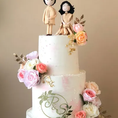 A close-up of the three-tiered engagement cake, showing the custom couple topper and monogram.