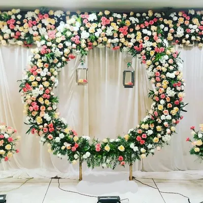 This stunning engagement stage features a full ring of multi-colored roses against a clean white backdrop. The symmetrical arrangement of floral bouquets on white pedestals adds to the elegance of the design.