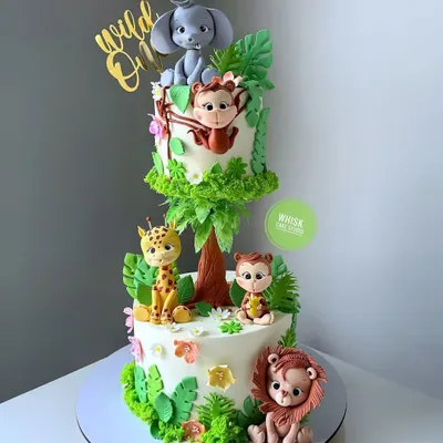 Go wild for this two-tiered jungle animal cake. This buttercream cake features adorable fondant animals like a lion, giraffe, and elephant, making it perfect for a "Wild One" first birthday.