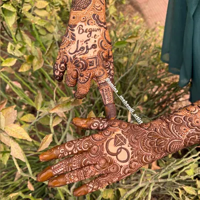 A close-up of a personalized engagement mehendi, featuring the bride's name 'Begum' and the groom's name in Urdu script, alongside a classic engagement ring symbol.