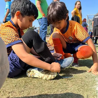 This is what teamwork looks like. A young player helps his teammate with his shoelaces, showing the camaraderie we build at our academy.