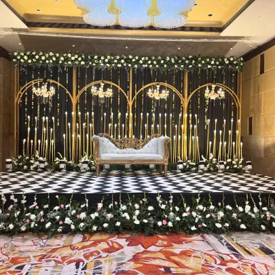 A chic Sangeet stage with a black and gold theme. The checkered dance floor, candle-lit backdrop, and elegant chandeliers create a sophisticated and glamorous atmosphere for performances.