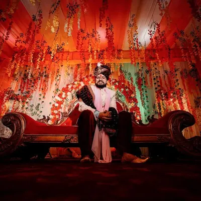 A powerful, wide-angle portrait of the groom seated on a royal sofa. The dramatic lighting and grand decor create a regal and commanding presence, fit for a king on his wedding day.