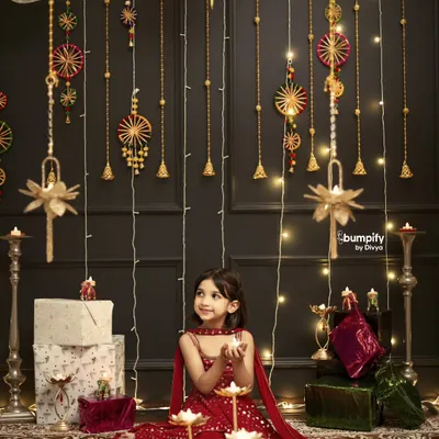 The magic of Diwali through a child's eyes. This little girl in her beautiful red dress is surrounded by the warm glow of diyas and festive decorations in our special Diwali studio setup.