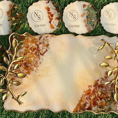 A complete wedding varmala preservation set, featuring a rectangular tray with elegant gold branch handles and eight matching coasters. The couple's initials and wedding date are inscribed on each piece, with their delicate varmala flowers preserved within the resin.