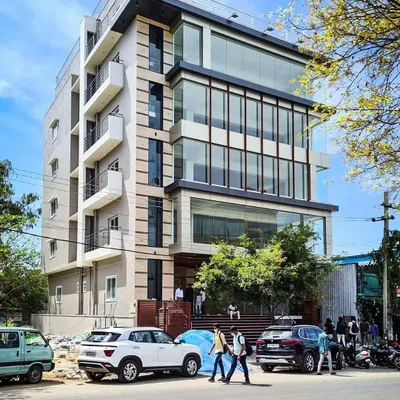 A street-level view of the completed commercial building in HSR Layout, occupied by brands like BlueStone. The design features a multi-level glass facade that creates a modern, transparent look for the office and retail spaces within.