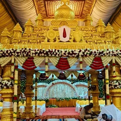 A magnificent golden mandap designed to look like a traditional temple gopuram. This grand setup, decorated with red and white floral garlands, is perfect for a classic South Indian wedding ceremony.