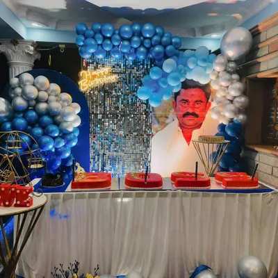 A full view of a highly personalized birthday setup. The key feature is the large custom portrait backdrop, complemented by a blue and silver balloon arrangement and a shimmer wall.