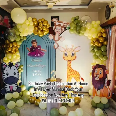 A cute jungle safari theme for a second birthday party at home. This setup features a custom arch backdrop, friendly animal cutouts like a lion and giraffe, and a green and gold balloon garland.