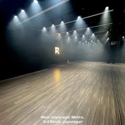 A wide shot of the Jayanagar studio, showcasing the dramatic overhead spotlights, polished wooden floors, and the glowing 'R' logo. The light haze from our smoke machine adds to the cinematic feel, making it an ideal setting for professional video shoots.