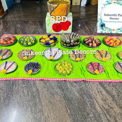 A large arrangement of seer plates filled with various sweets and savouries, ready for an engagement ceremony. The bright green cloth adds a pop of colour.