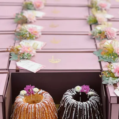 A close-up of our twin bundt cakes, a popular choice for return favours. This set includes one vanilla and one chocolate cake, both drizzled with icing and topped with delicate fresh flowers, ready to be gifted in our custom pink boxes.