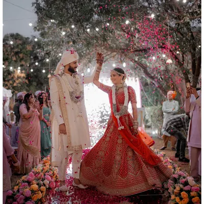 A magical moment from Miti and Dharmil's Gujarat wedding. The couple stands on a mirrored stage, showered with rose petals under a canopy of lights, creating a truly cinematic frame.