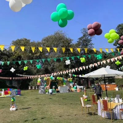 A wide view of a large-scale jungle themed party on a sunny day, showing guest seating, food stalls, and the main stage area.