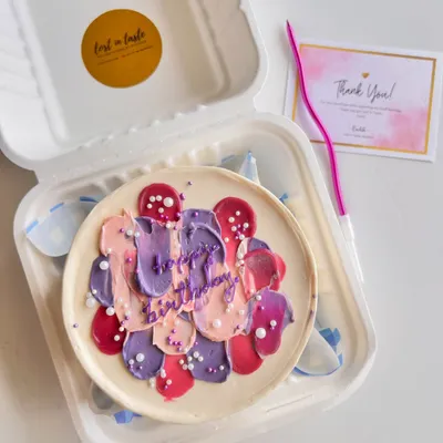 An abstract birthday bento cake featuring textured buttercream strokes in shades of purple, pink, and peach, finished with a sprinkle of white pearls for a modern, artistic feel.