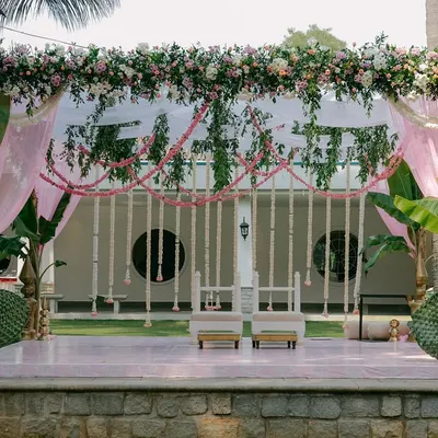 A full view of the mandap for a South Indian morning wedding, featuring blush pink drapes, traditional jasmine and tuberose garlands, and sacred banana trees framing the stage.