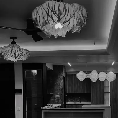 A study in sculptural lighting. This black and white photo highlights the different forms and textures of light fixtures in one of our projects, from folded paper-like shades to undulating wooden pendants, each adding a layer of artistry to the ceiling.
