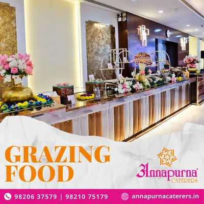 We now offer modern grazing food tables for a more interactive dining experience. This image shows an elaborate setup with a variety of appetizers and desserts, beautifully arranged with floral decorations on our stylish counters.