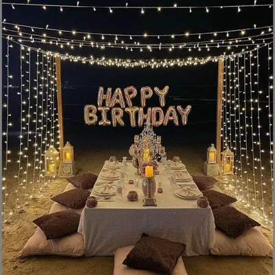 A dream-like birthday dinner setup on the beach. We created a canopy of fairy lights over a low-seating dining table, with "Happy Birthday" foil balloons and lanterns creating a magical atmosphere.