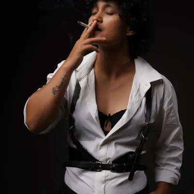 A moody studio portrait from the "Leather straps and Cigarettes" series. The dark background and single light source create a dramatic, film-noir atmosphere.