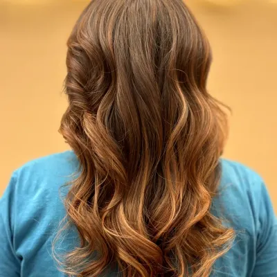 A stunning example of a balayage or ombré effect, with dark roots melting into lighter ends. The hair is styled in loose curls to perfectly showcase the color transition.