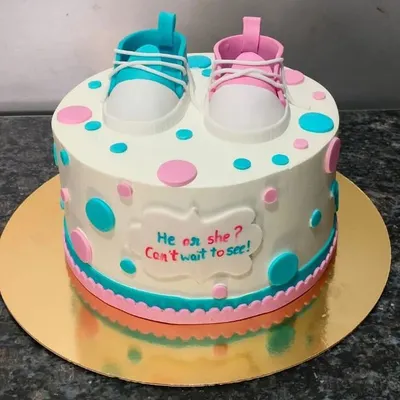 "He or she? Can't wait to see!" This is a classic gender reveal cake, decorated with pink and blue baby shoes and polka dots. The inside holds the sweet secret.