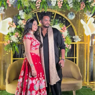 A stylish couple at their Sangeet night. The decor features a modern gold grid backdrop, pastel floral arrangements, and glowing butterfly motifs.