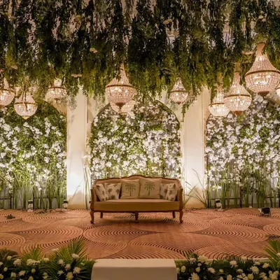This reception stage combines a lush overhead canopy of greenery and crystal chandeliers with dense floral walls, creating a breathtaking focal point for the evening's celebrations.