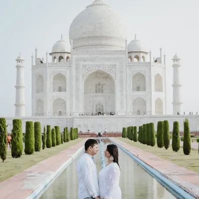 A classic, symmetrical shot of a couple at the Taj Mahal. Dressed in white, they complement the serene beauty of the monument, creating a powerful and iconic pre-wedding photograph.