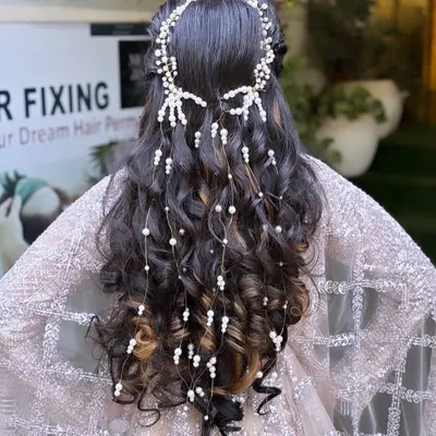 Your hairstyle is just as important as your makeup. This intricate look features cascading curls adorned with delicate pearl accessories, creating a romantic and sophisticated style perfect for an engagement or wedding.