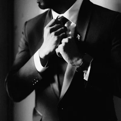 A moody and classic black and white shot of a groom adjusting his tie. This close-up focuses on the details and the sense of anticipation, creating a powerful and timeless image.