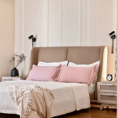 This serene bedroom features a winged headboard and fluted wall paneling in a light wood finish. The combination of soft textures, gentle colors, and adjustable wall sconces creates a perfect environment for relaxation.