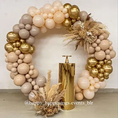 A full circular balloon arch makes a spectacular photo backdrop. This design uses a sophisticated palette of beige, brown, and chrome gold, accented with dried florals and pampas grass for a modern, earthy feel.