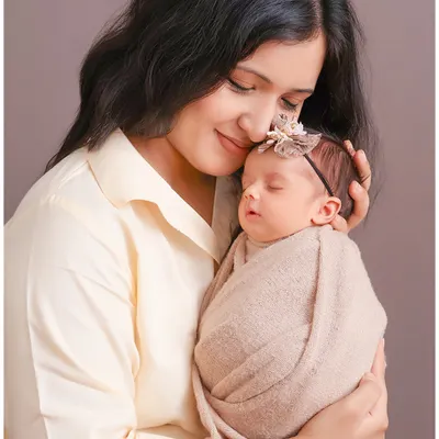 This portrait captures the quiet, protective love of a new mother. The soft lighting and the gentle embrace highlight the tender bond and the peacefulness of a sleeping newborn.