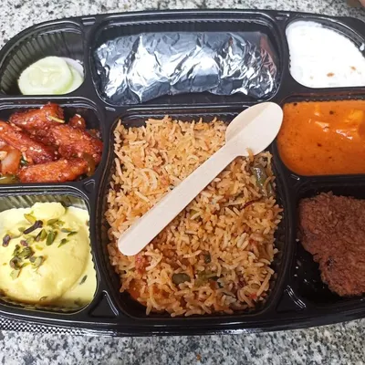 Seasoned rice sits at the centre of this meal tray we pack with curry, a starter, cucumber, bread and sweets.