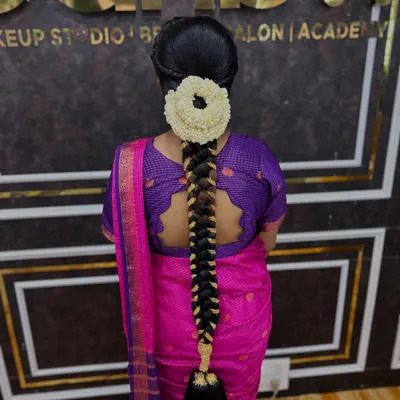 A classic South Indian bridal braid, neatly woven and adorned with a round arrangement of fresh jasmine flowers. This style is timeless and elegant.