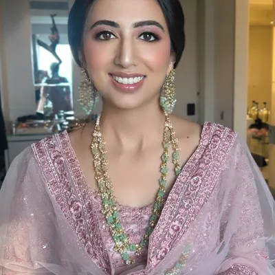 A happy and radiant wedding guest in a beautiful pink embroidered outfit. We created a fresh, glowing makeup look with pink tones and styled her hair in a sleek low bun to complement her elegant attire.