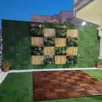 A beautiful green wall design combining an artificial grass base with bamboo panels and planter boxes for a textured, natural look. The wooden deck flooring provides a perfect yoga or seating spot.