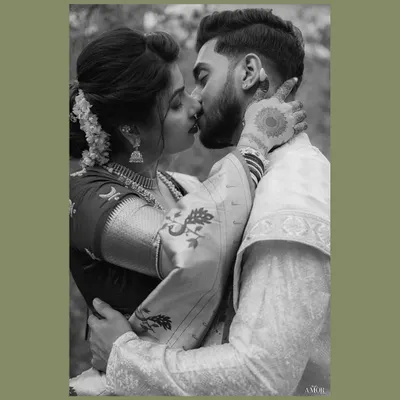 An intimate black and white portrait capturing a gentle kiss. The focus on the bride's traditional jewelry and the groom's tender embrace highlights the romantic essence of a Maharashtrian couple shoot.