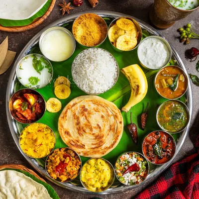 A magnificent South Indian thali served on a banana leaf, featuring a colorful assortment of curries, rice, parotta, and sweets, captured from above to showcase the entire spread.