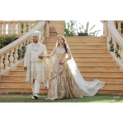 A picture of pure elegance. The couple makes their entrance in coordinated ivory and gold outfits. The bride's Tarun Tahiliani lehenga and the groom's Shantanu & Nikhil sherwani create a perfectly synchronized, regal statement for their wedding day.