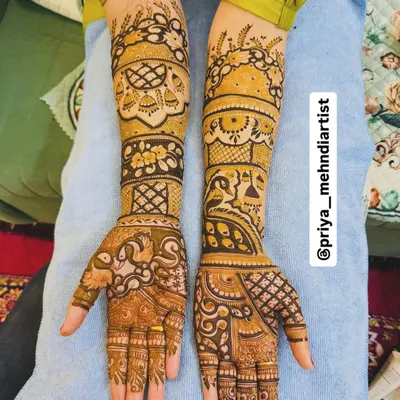 A classic full bridal mehndi design featuring traditional motifs like kalash and peacocks, covering the arms from elbow to fingertips with dense, detailed patterns.