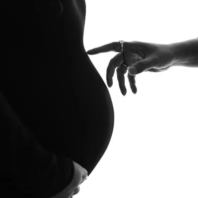 A fine art-inspired silhouette, reminiscent of Michelangelo's "Creation of Adam." This close-up on the simple touch between a partner's hand and the baby bump is incredibly powerful and symbolic.